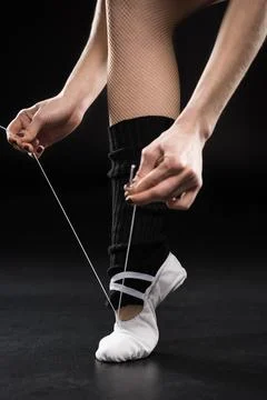 Close-up partial view of woman dancer tying ballet shoe on black Stock Photos