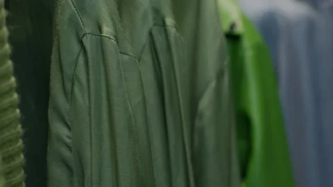 A close-up of the passage of clothes hanging on a rail in green and blue colors Видео 267625936