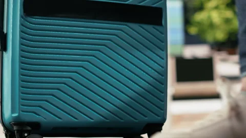 Close up of passenger pulling trolley luggage across bus terminal waiting area Stock Footage 340202181