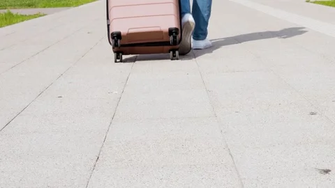 Close-up of a passenger walking, pulling a pink suitcase on wheels. This tourist Stock Footage 339273569