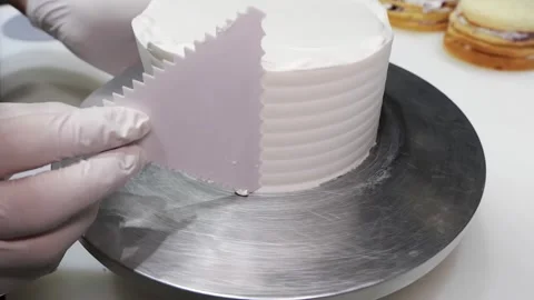 Close-up of Pastry Chef Decorating White Cream Cake with a Scraper Tool on a Rot Stock Footage 331777960
