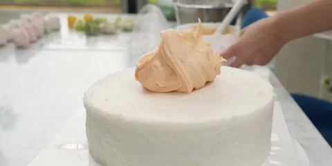 Close-up of Pastry Chef Spreading Pastel Orange Buttercream Frosting on White Ce 스톡 동영상 343589327