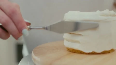 Close-up of a pastry chef turns the table and smears the cake with whipped cream Stockbeeldmateriaal 196010197