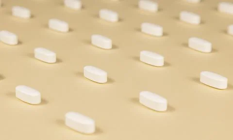 Close-up of a pattern of white pills on a beige background. Stock Photos