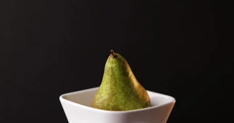 Close-up pear turning in bright white bowl on deep black studio background Stock Footage 320408601