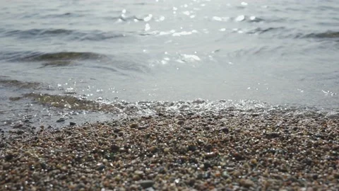 Close-up of pebble beach with transparent waves with sun glare on the water. Stock Footage 205816140