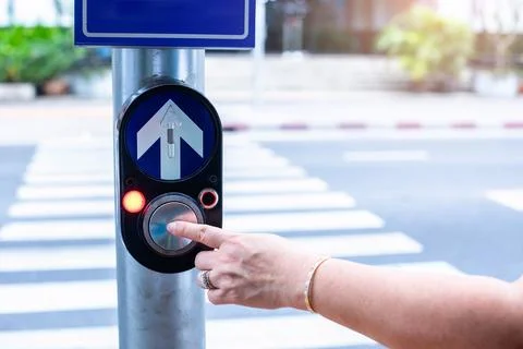 Close up pedestrian crossing call button. Hand pushing button to cross. The.. Stock Photos