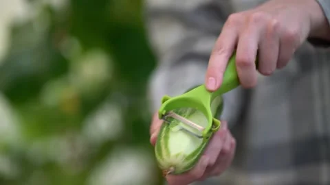 Close-up of peeling a cucumber with a green vegetable peeler in natural ligh Vídeos de archivo 341903242
