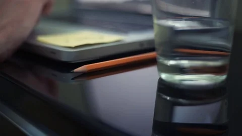 Close up pencil on table. Defocused objects glass of water, male hands on laptop Stock Footage 82934924