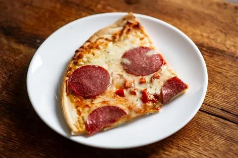 Close-up of pepperoni pizza slice on white plate on rustic wooden table Stock Photos