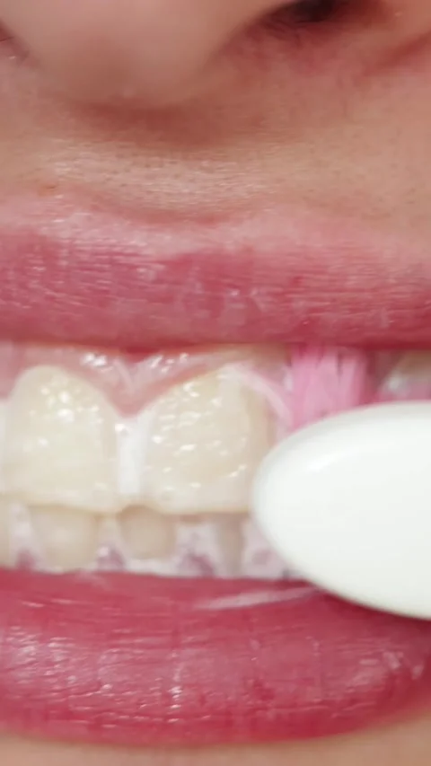 Close-up of person brushing teeth with pink toothbrush and white paste Stockbeeldmateriaal 343838028