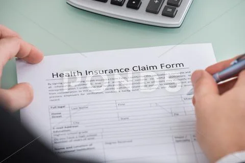 Close-Up Of Person Filling Health Insurance Claim Form
