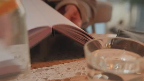 Close up of person flipping through open book on textured table with glass Stock Footage 345065932
