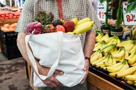 Close up of person at a food and vegetable market, holding shopping bag with Stock Photos