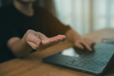 Close-up of person gesturing with hand while using laptop on wooden table i.. Stock Photos