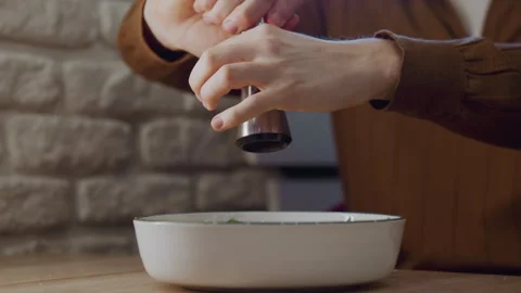 Close up of person grinding pepper over bowl in kitchen with stone wall 動画素材 345731717