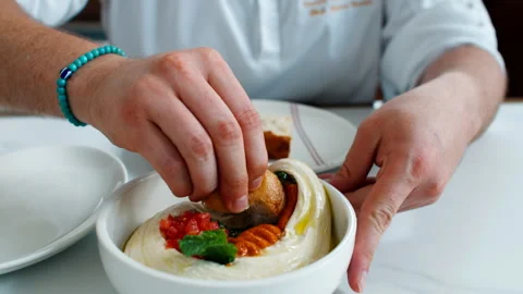 Close up of a person hand dipping a piece of crusty bread into a white ceramic Stock Footage 336936007