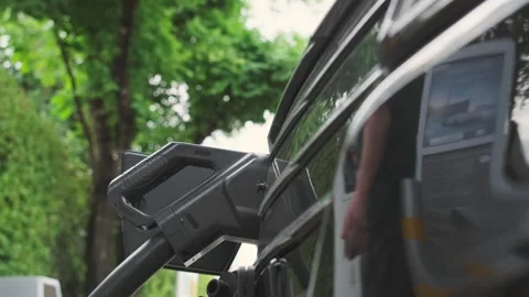 A close-up of a person holding a charging plug near an electric vehicle. Stock Footage 314770783