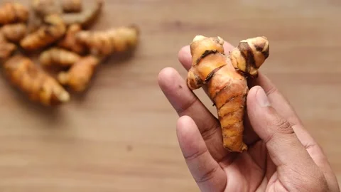 Close up of person holding fresh raw turmeric root over wooden table in slo.. Stock Footage 333031153