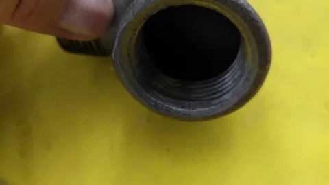 Close-up of a person holding a metal threaded pipe elbow fitting over a yellow b Stock Footage 337052652