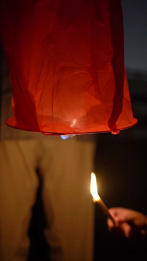Close-up of a person lighting a red paper sky lantern with a candle before Stock Footage 340074098
