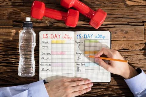 Close-up Of A Person Making Exercise Plan On Notebook Over Wooden Desk Foto stock
