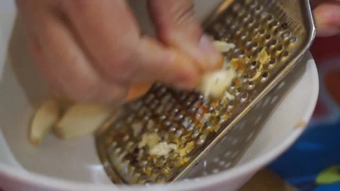 A close-up of a person manually grating garlic using a traditional grater Video stock 323939022
