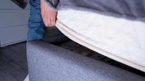 Close-up of a person placing a stack of US dollar bills under a mattress Stock Footage 310007795