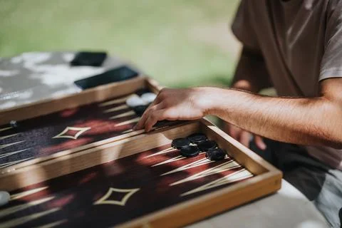 Close-up of a person playing backgammon outside, focusing on hands moving pieces Stock Photos