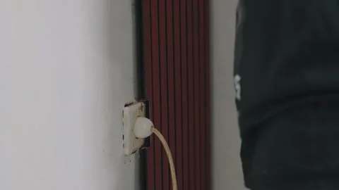 Close-up of a person plugging a cord into an old, worn electrical wall socket Stock Footage 333321443