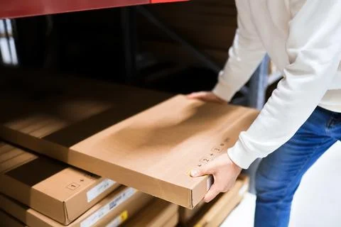 Close-up of a person pulling a flat-pack cardboard box from a shelf in a la.. Stock Photos