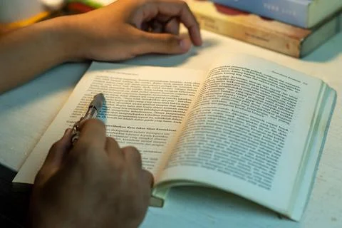 Close-up of a person reading a book while holding a pen Stock Photos