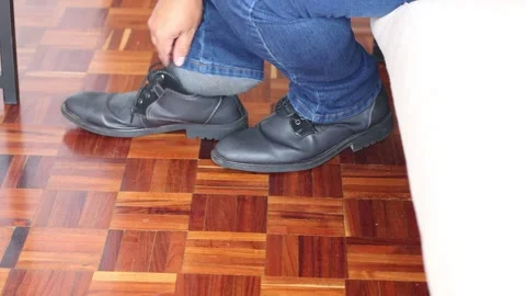 Close-up of a person sitting on a sofa, tying dress shoes on a wooden floor.. Stock Footage 301105682