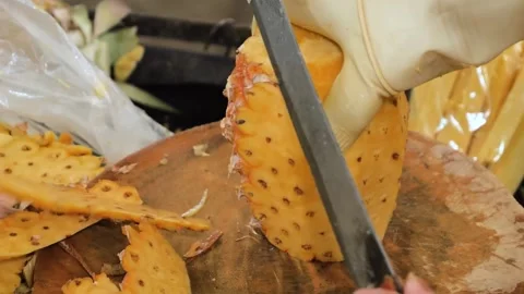 Close-up of a person slicing the outer skin off a ripe pineapple on a wooden cut Stock Footage 345635863