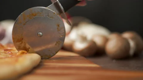 Close-up of a person slicing a pizza into multiple slices with a cutter. Stock Footage 137479262