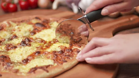 Close-up of a person slicing a pizza into multiple slices with a cutter. Stock Footage 137485433