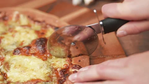 Close-up of a person slicing a pizza into multiple slices with a cutter. Stock Footage 137485453