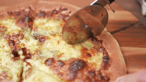 Close-up of a person slicing a pizza into multiple slices with a cutter. Stock Footage 137485535