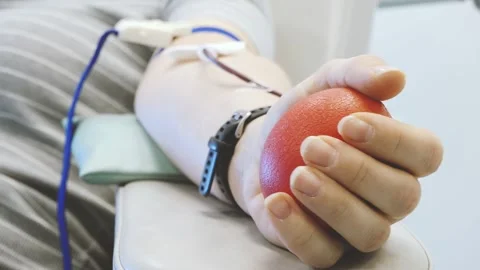 Close-up of a person squeezing a red stress ball while donating blood Stock Footage 329627640