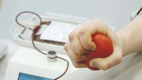 Close-up of a person squeezing a red stress ball while donating blood, with Stock Footage 331213636