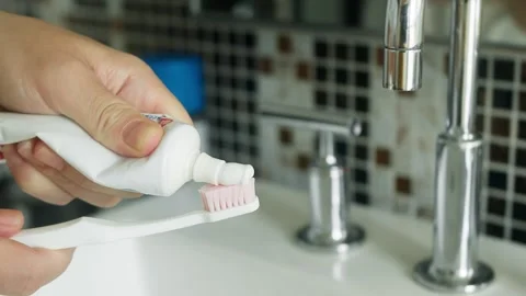 Close-up of a person squeezing toothpaste from a tube onto the bristles of a Видео 346404896