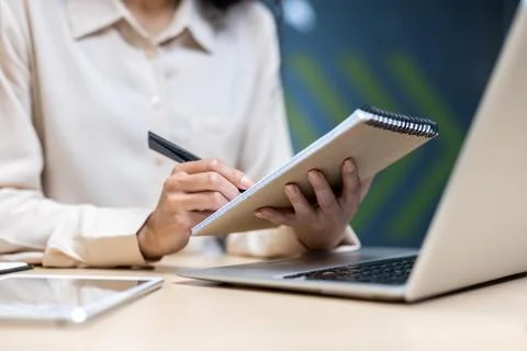 Close-up of person taking notes in notebook while working on laptop at office Stock Photos