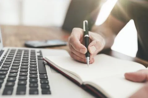 Close-up of person taking notes with pen on paper in front of laptop computer Stock Photos