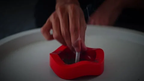 Close-up of person tapping cigarette in red lips-shaped ashtray on white table Stock Footage 316887518