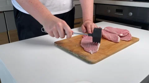 Close-up of a person using a black meat mallet to pound pork cutlets on a w.. Stock Footage 320955243