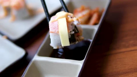 Close up of person using chopsticks to carefully dip sushi roll into soy sauce Stock Footage 326464110