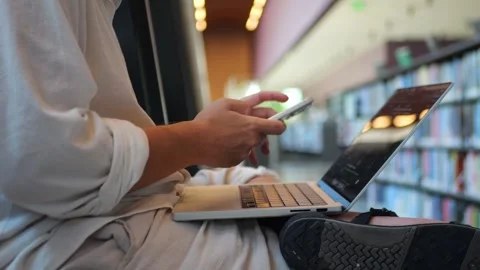 Close-Up of Person Using Smartphone Beside Laptop in Library... Vídeo Stock 334437002