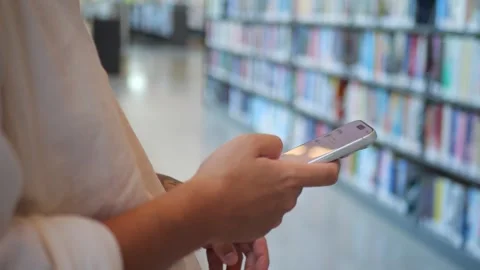 Close-Up of Person Using Smartphone In Library, Representing... 動画素材 334437086