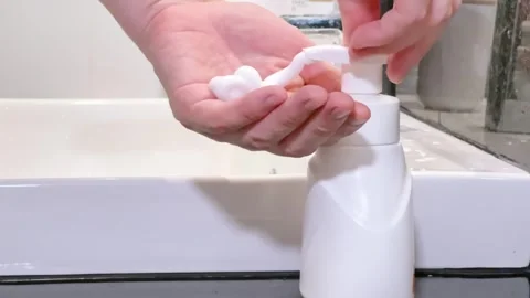 Close-up of a person using a white foam soap dispenser in a white bathroom sink Stock-Footage 276818731