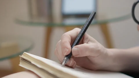 Close up of a person writing in a notebook with a black pen, focusing on the Stock Footage 341035135